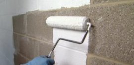 Rolling masonry sealer on basement walls.